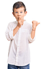 Cute blond kid wearing elegant shirt asking to be quiet with finger on lips pointing with hand to...