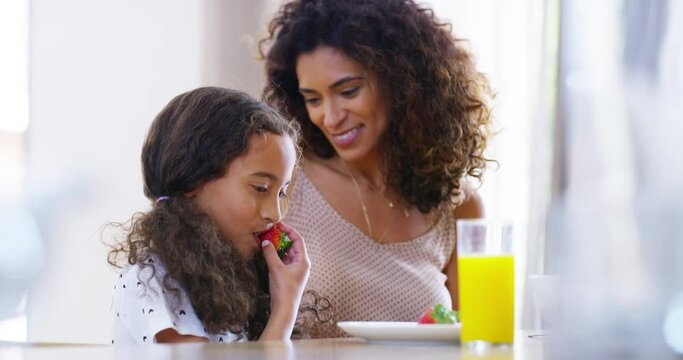 Family, breakfast child with mother eating strawberry fruit together and hugging by their kitchen table at home. Smile, love and happy little girl sharing her food with her parent with care