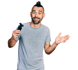 Hispanic man with ponytail holding electric razor machine celebrating achievement with happy smile and winner expression with raised hand
