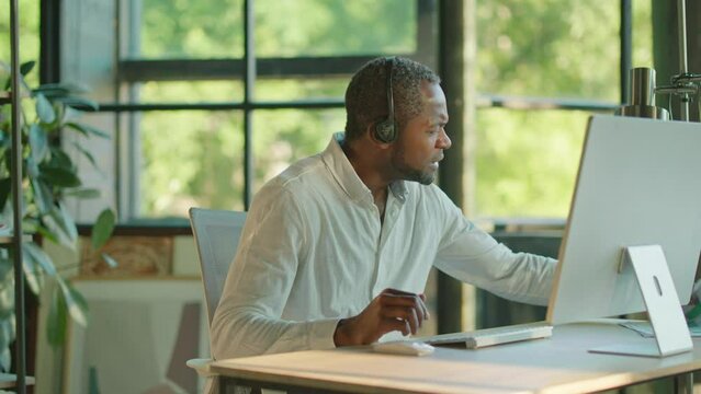 View of african american businessman holds documents using a headset to make a conference video call on a laptop in a light office. Communication. Talking. Slow motion