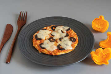 Halloween mini pizza for kid's snack on dark plate. on the background of wooden cutlery and traditional decorations.