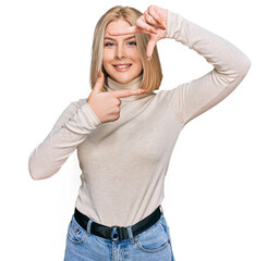 Young blonde woman wearing casual clothes smiling making frame with hands and fingers with happy face. creativity and photography concept.