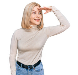 Fototapeta premium Young blonde woman wearing casual clothes very happy and smiling looking far away with hand over head. searching concept.