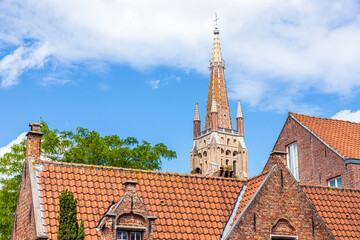 Fototapeta premium The spire of the Church of Our Lady (Onze-Lieve-Vrouwekerk) overlooking pantiled rooves of old houses in Bruges, Belgium