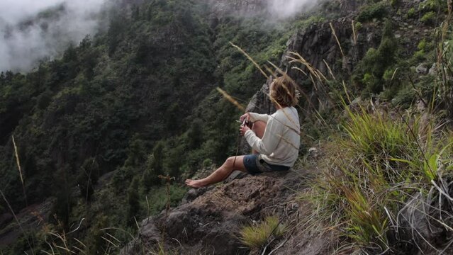 Man artist sits down on rock on top of a foggy mountain and opens his notebook