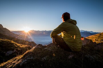 Man sitting on a top of mountain and watching the sunset