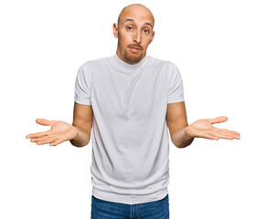 Bald man with beard wearing casual white t shirt clueless and confused expression with arms and...