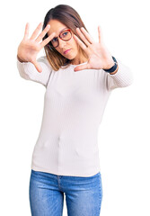 Obraz na płótnie Canvas Beautiful brunette young woman wearing casual white sweater and glasses doing frame using hands palms and fingers, camera perspective