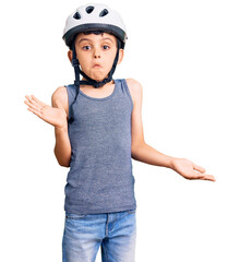 Little cute boy kid wearing bike helmet clueless and confused expression with arms and hands raised. doubt concept.