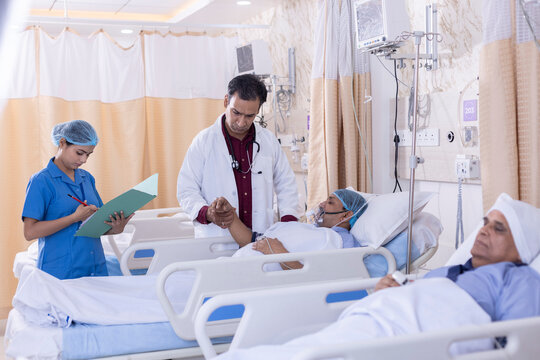 Nurse with male doctor examining of patient lying on icu bed at hospital
