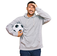 Handsome man with tattoos holding soccer ball stressed and frustrated with hand on head, surprised...