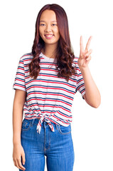 Young beautiful chinese girl wearing casual clothes smiling with happy face winking at the camera doing victory sign. number two.