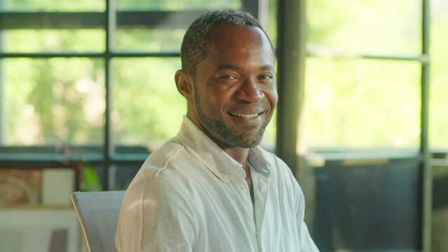 Portrait of a happy african american man turns his head to look at the camera smiling. Sitting in office. Businessman, entrepreneur, CEO. Corporate business. Slow motion