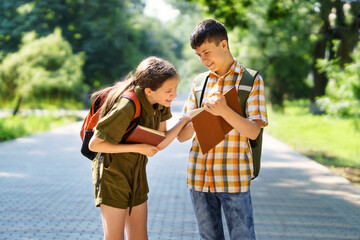 portrait of students in a city park, teenage schoolchildren a boy and a girl are standing on the path and discussing lessons, reading a book and talking