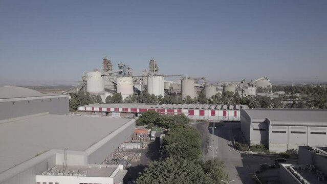 Aerial shot of a huge cement factory, an innovative industrial area with lots of hangars and trucks, a beautiful area with trees, push in shot