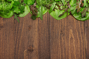top view of green dill, parsley, salad, herbs and other greens on a dark wooden background, concept of fresh vegetables and healthy food, blank space or copy space for text