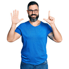 Hispanic man with beard wearing casual t shirt and glasses showing and pointing up with fingers number seven while smiling confident and happy.
