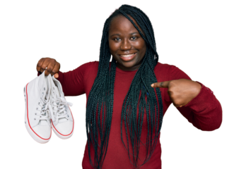 Young black woman with braids holding casual shoes pointing finger to one self smiling happy and proud