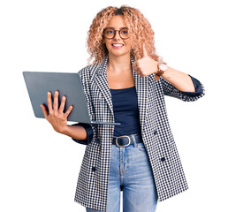 Young blonde woman with curly hair working using laptop smiling happy and positive, thumb up doing...