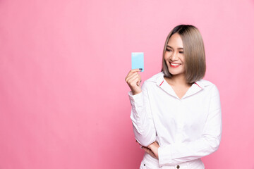 Shopping concept. Young Asian woman smiling and showing plastic credit card, paying contactless, standing over pink background