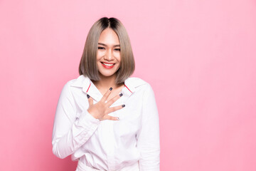 Lovely young woman presses palms to heart, feels touched and grateful, looks with admiration at something, keeps all good memories, dressed in white shirt, isolated over pink background