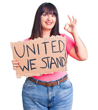 Young Plus Size Woman Holding United We Stand Banner Doing Ok Sign With Fingers, Smiling Friendly Gesturing Excellent Symbol