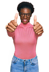 Young african american girl wearing casual clothes and glasses approving doing positive gesture with hand, thumbs up smiling and happy for success. winner gesture.