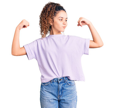 Beautiful Kid Girl With Curly Hair Wearing Casual Clothes Showing Arms Muscles Smiling Proud. Fitness Concept.