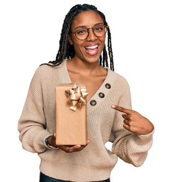 African american woman holding gift smiling happy pointing with hand and finger