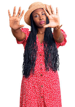 Young african american woman wearing summer hat doing frame using hands palms and fingers, camera perspective