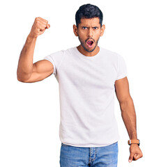 Young latin man wearing casual clothes angry and mad raising fist frustrated and furious while shouting with anger. rage and aggressive concept.