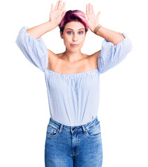 Young beautiful woman with pink hair wearing casual clothes doing bunny ears gesture with hands palms looking cynical and skeptical. easter rabbit concept.