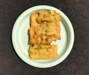 Tempe Goreng is an Indonesian food made from fermented soybeans and then fried using flour. Photographed on a green plastic plate isolated on a dark background
