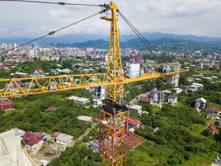 Close-up of a yellow construction crane on the background of mountains, private sector on a sunny day, view from a drone