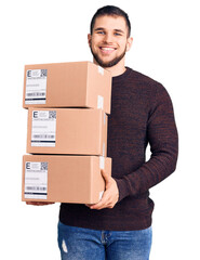 Young handsome man holding delivery package looking positive and happy standing and smiling with a...