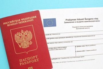 Schengen visa application form in Russian and Lithuanian language and passport on blue background....