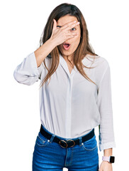 Young caucasian girl wearing casual white shirt peeking in shock covering face and eyes with hand, looking through fingers with embarrassed expression.