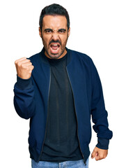 Young hispanic man wearing casual clothes angry and mad raising fist frustrated and furious while shouting with anger. rage and aggressive concept.