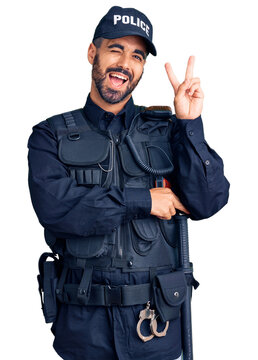 Young hispanic man wearing police uniform smiling with happy face winking at the camera doing victory sign with fingers. number two.
