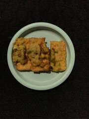 Tempe Goreng is an Indonesian food made from fermented soybeans and then fried using flour. Photographed on a green plastic plate isolated on a dark background