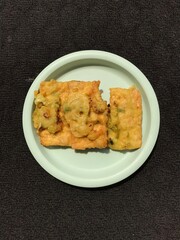 Tempe Goreng is an Indonesian food made from fermented soybeans and then fried using flour. Photographed on a green plastic plate isolated on a dark background
