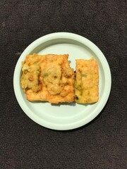 Tempe Goreng is an Indonesian food made from fermented soybeans and then fried using flour. Photographed on a green plastic plate isolated on a dark background