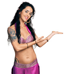 Young indian woman wearing belly dancer costume inviting to enter smiling natural with open hand