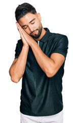 Young man with beard wearing sportswear sleeping tired dreaming and posing with hands together while smiling with closed eyes.