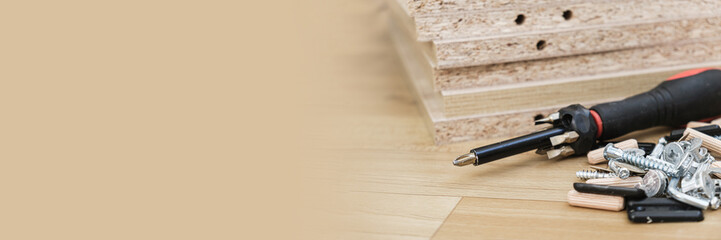 Screwdriver with removable nozzles and parts for assembling furniture on parts of cabinet furniture made of laminated chipboard background. Self-assembly of cabinet furniture. Banner, space for text