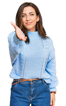 Young brunette woman wearing casual winter sweater smiling cheerful offering palm hand giving assistance and acceptance.