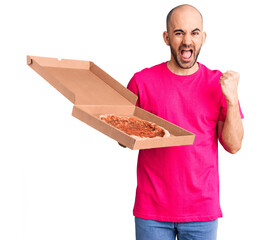 Young handsome man holding delivery pizza cardboard box screaming proud, celebrating victory and success very excited with raised arms