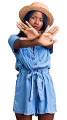 Young indian girl wearing summer hat rejection expression crossing arms and palms doing negative sign, angry face