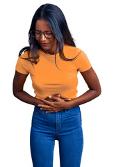 Young indian girl wearing casual clothes and glasses with hand on stomach because indigestion, painful illness feeling unwell. ache concept.