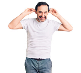 Middle age handsome man wearing casual t-shirt smiling pulling ears with fingers, funny gesture. audition problem